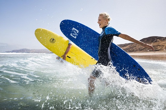 Frau läuft mit Surfbrett ins Meer zum Surfen auf Fuerteventura