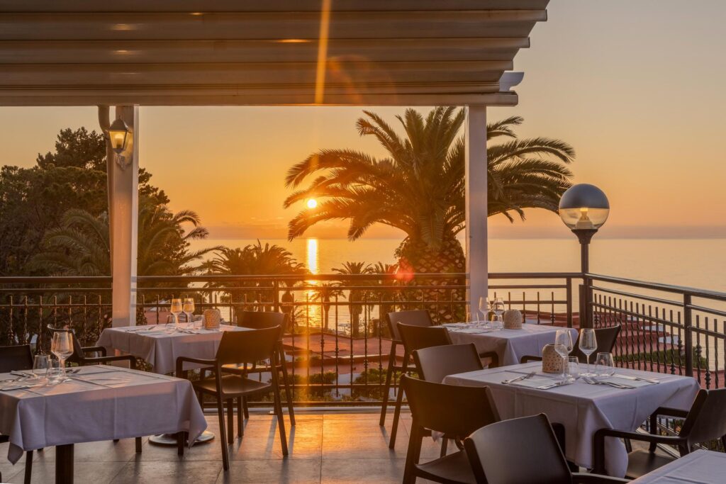 Restaurantterrasse des Aldiana Club Rocca Nettuno mit traumhaftem Blick auf das Meer, während die Sonne untergeht.