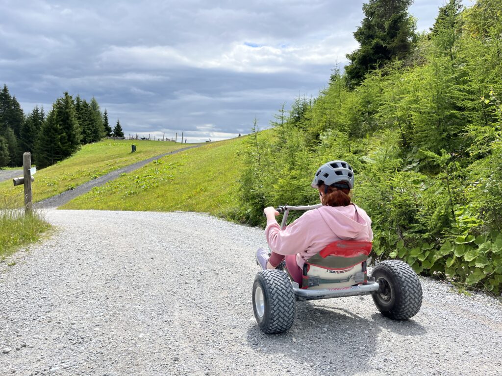 Eine Frau fährt mit einem Mountain Cart auf einem Schotterweg.  