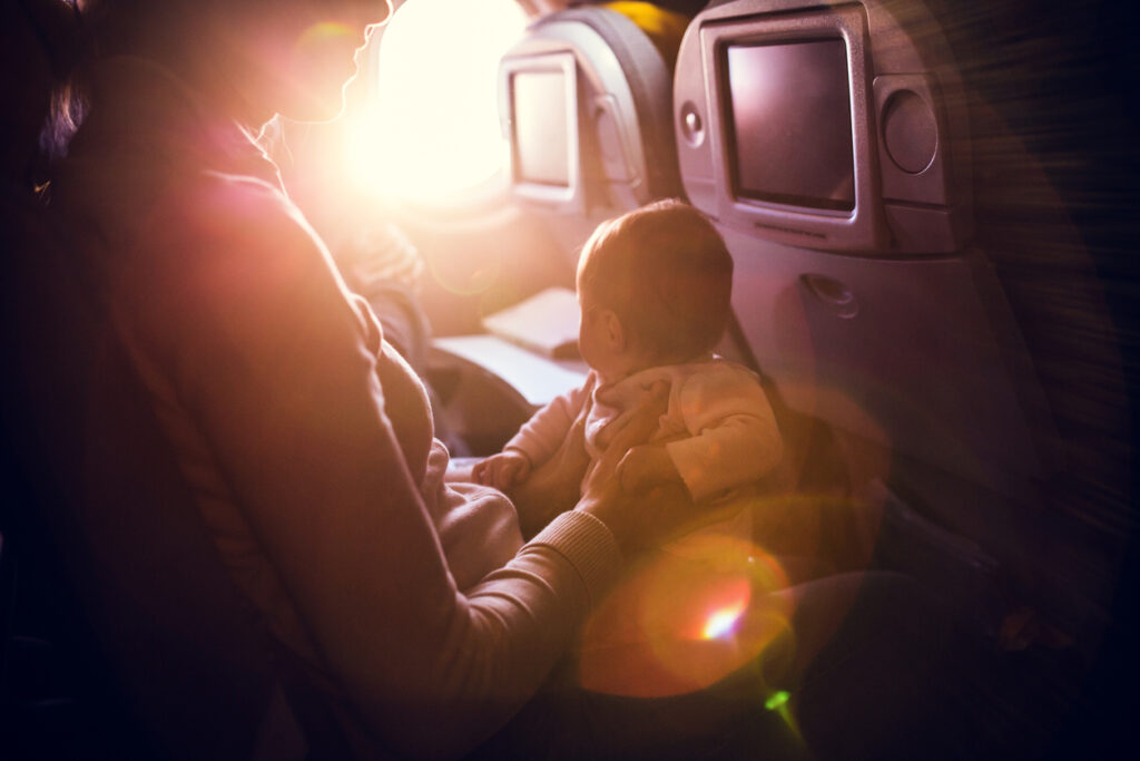 Baby auf dem Schoß der Mutter in einem Flugzeug. In dieser Haltung kann auch gut Babynahrung im Flugzeug zu sich genommen werden. 