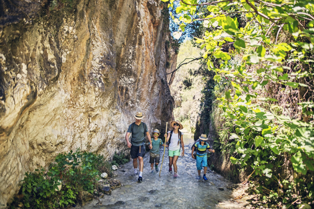 Vater und Kinder wandern in Andalusien, Spanien. Sie gehen den Bergfluss in einer wunderschönen Schlucht hinauf.