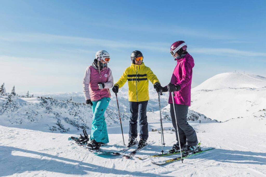 Zwei Skifahrer und eine Snowboarderin stehen auf dem Berg in den Alpen zur Abfahrt bereit.