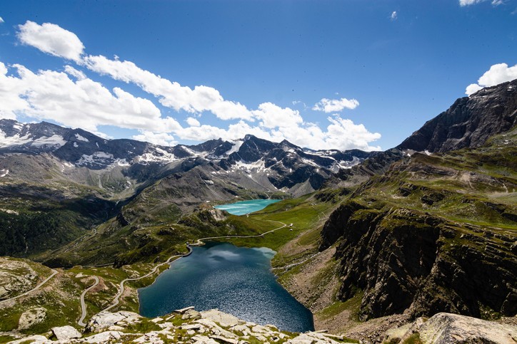 eine verschneite Berglandschaft im Hintergrund mit türkisenen Seen und viel grüner Landschaft
