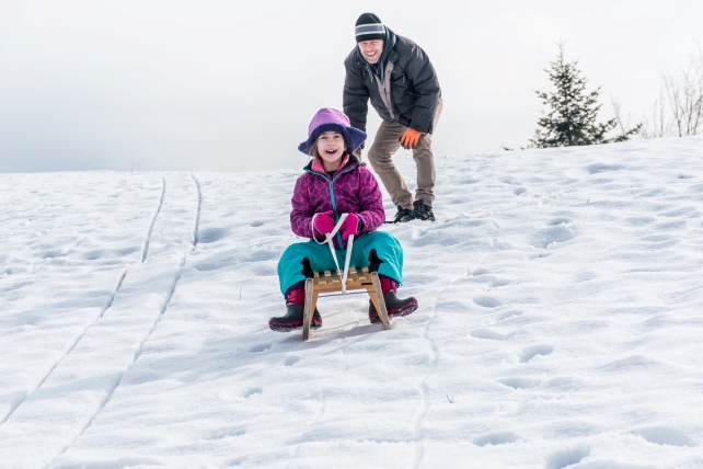 Schneelandschaft. Vater schiebt seine Tochter auf einem Schlitten den Weg hinunter