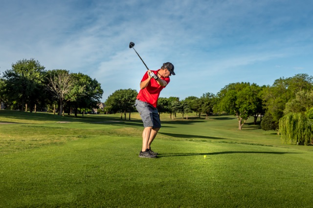 Ein Golfer im roten Shirt schwingt seinen Schläger auf einem grünen Golfplatz.