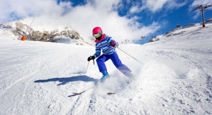 Kind fährt Ski auf einer sonnigen Piste in den Bergen.