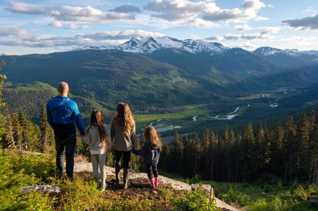 Familie genießt den Blick auf das grüne Tal und die schneebedeckten Berge.