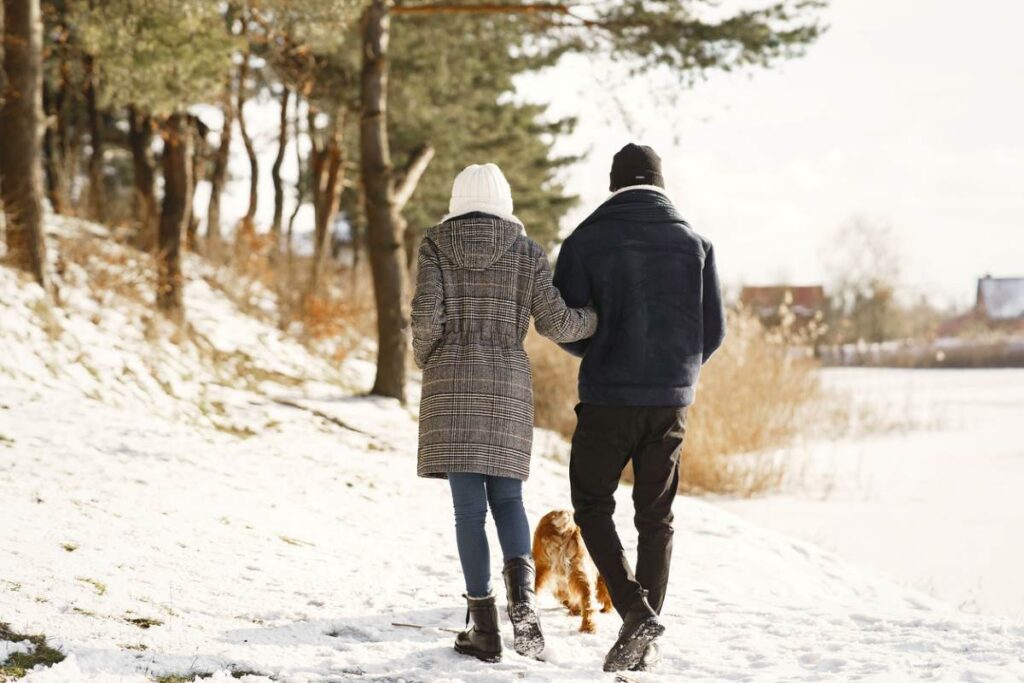 Paar macht einen Winterspaziergang mit Hund im verschneiten Wald.