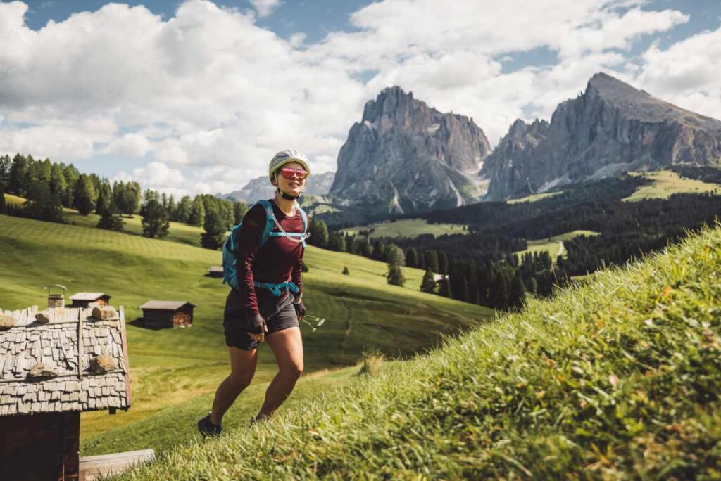 Frau wandert in alpiner Landschaft mit grünen Wiesen und hohen Bergen.