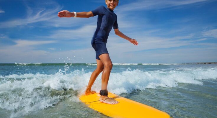 Kind in Neoprenanzug surft bei sonnigem Wetter auf kleinen Wellen.