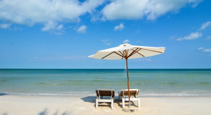 Zwei Liegestühle und ein Sonnenschirm am Strand mit Blick auf das Meer