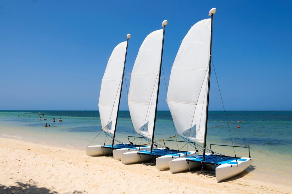 Drei Segelboote am Sandstrand bei klarem, blauem Himmel und ruhigem Meer.