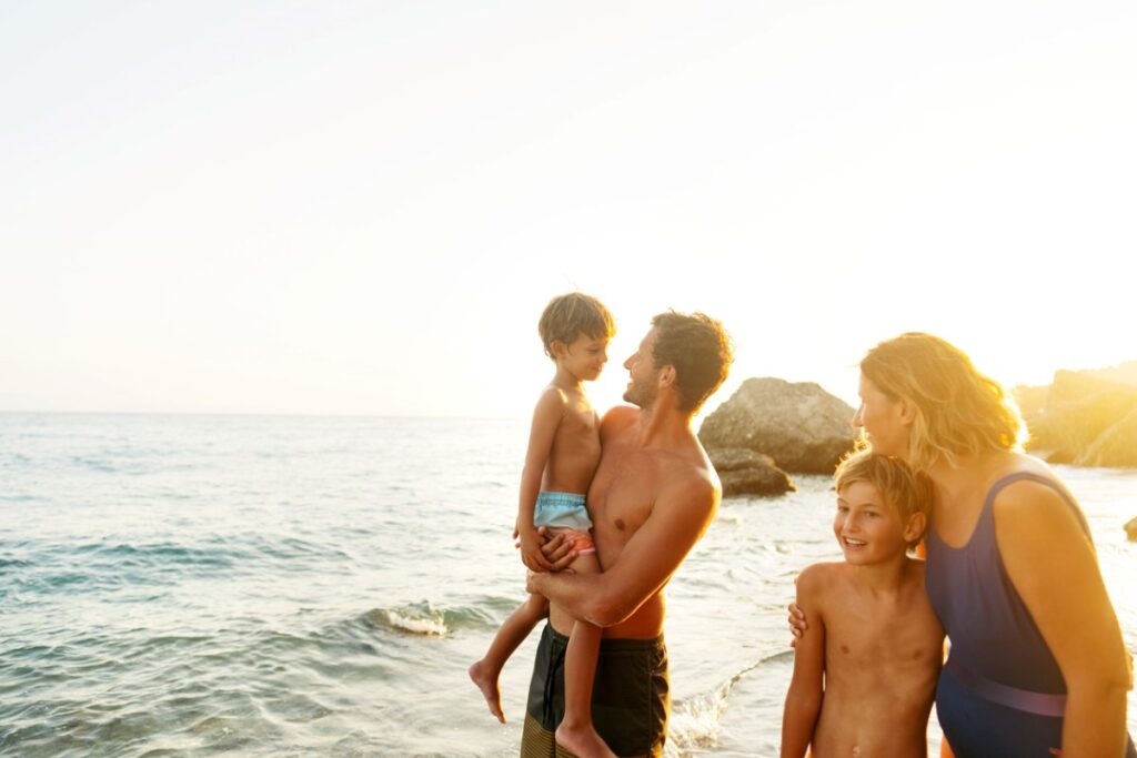 Eltern und Kinder lachen am Strand in der Abendsonne.