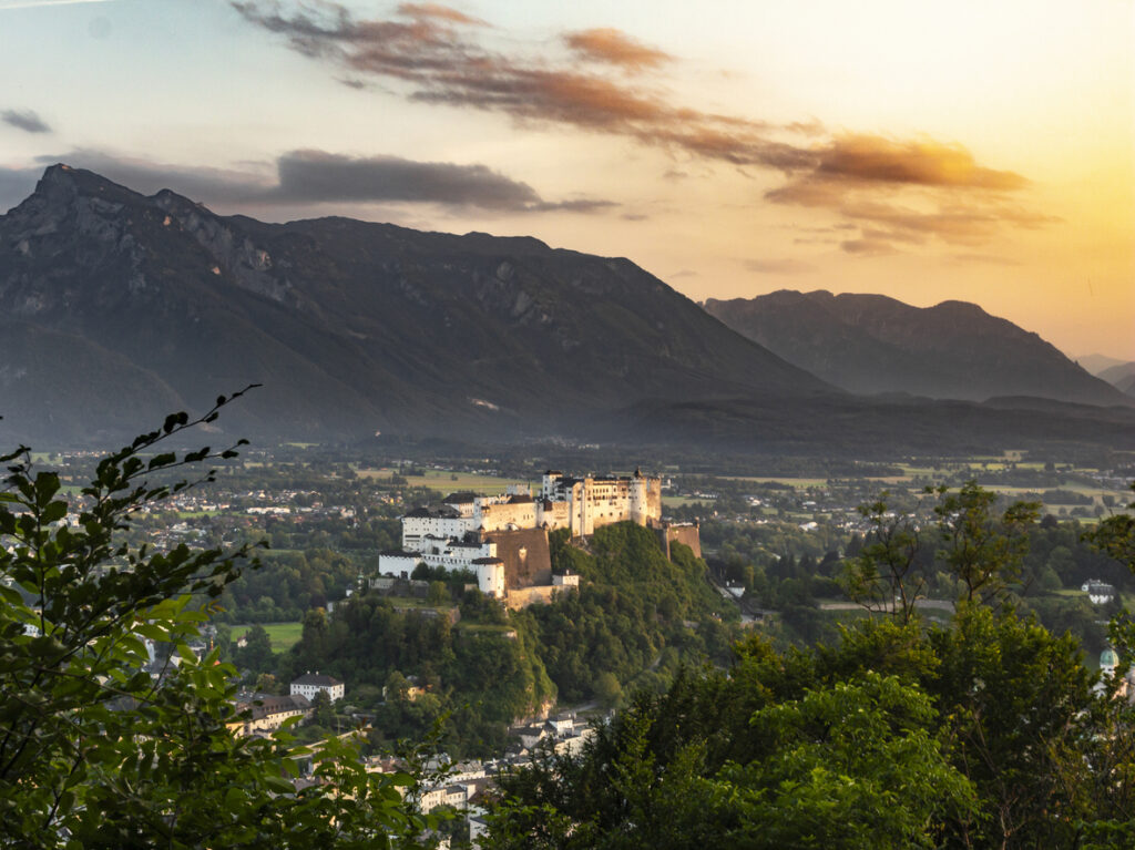Blick vom Kapuzinerberg in Salzburg, mit Schloss und Alpenbergen im Hintergrund bei Sonnenuntergang