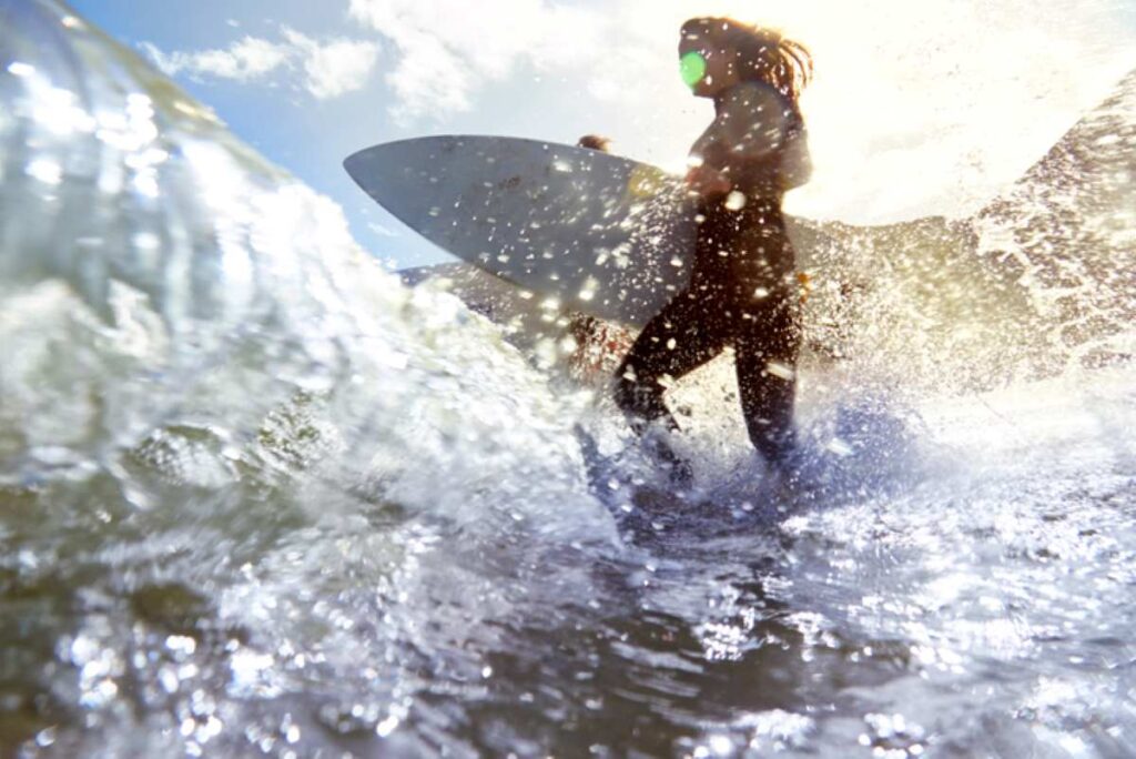 Frau mit Surfbrett im Sonnenlicht, umgeben von spritzendem Wasser.
