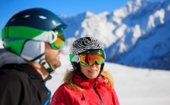 Zwei Skifahrer in bunten Helmen und Skibrillen vor schneebedeckten Bergen.