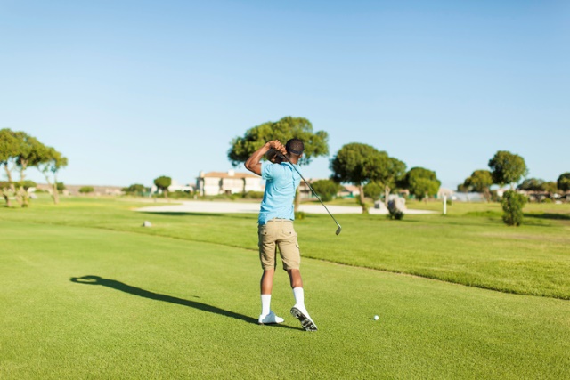 Mann golft auf einem schönen Golfplatz unter blauem Himmel.
