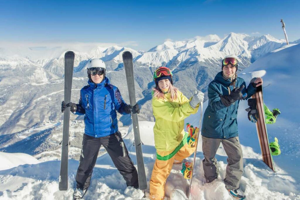 Gruppe von Skifahrern und Snowboardern posiert auf einem verschneiten Berggipfel.