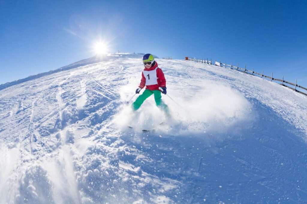 Kind in bunter Skiausrüstung fährt einen schneebedeckten Hang hinunter.