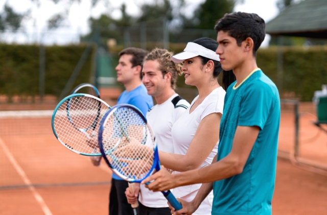 Vier Tennisspieler halten ihre Tennisschläger und stehen nebeneinander auf einem Tennisplatz.