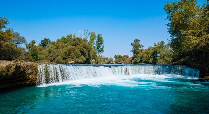 Kleiner Wasserfall mit klarem blauem Wasser und umgebenden Bäumen.