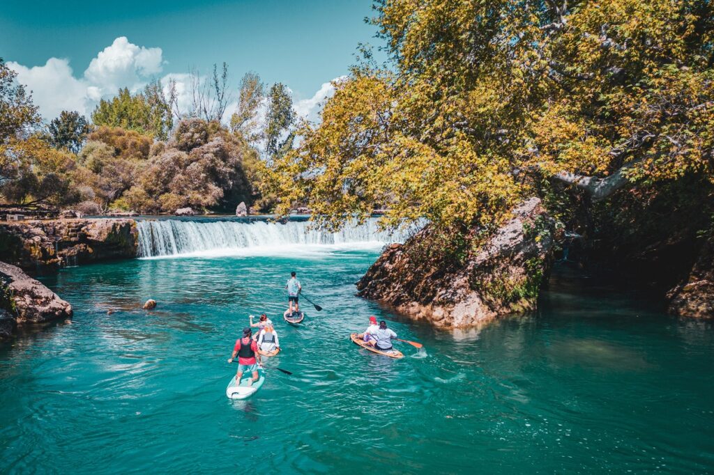 Menschen paddeln auf Stand-Up-Paddle-Boards auf dem türkisfarbenen Fluss vor dem Manavgat Wasserfall in der Türkei.