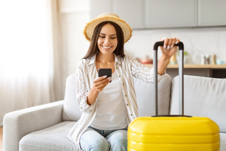 Frau checkt Packliste für den Sommerurlaub neben ihrem Koffer