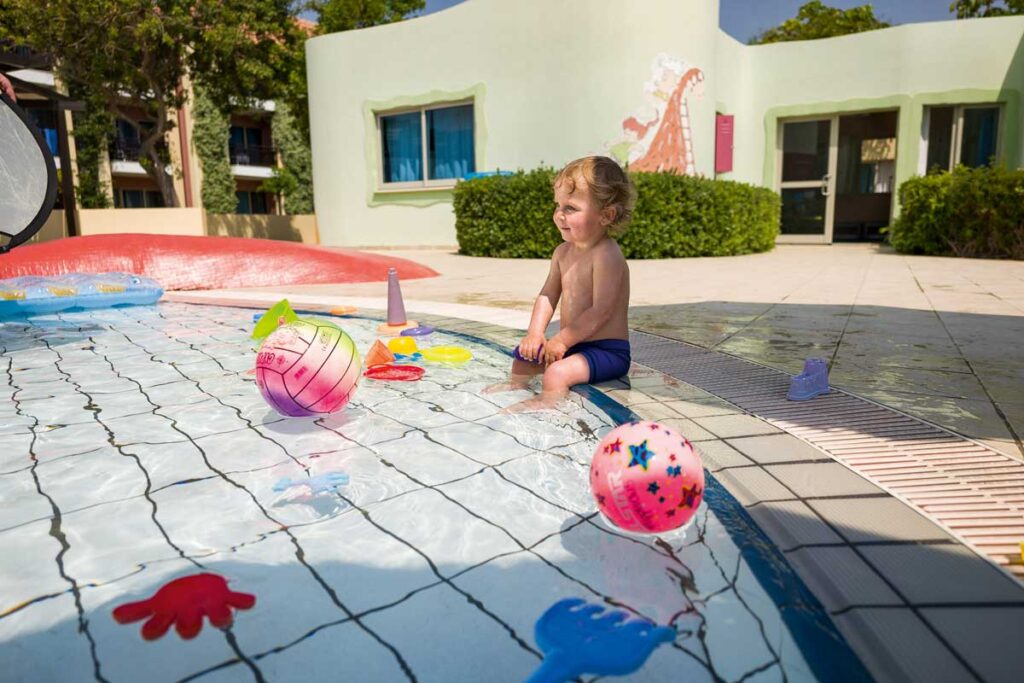 Kind sitzt im Pool mit Spielsachen die auf einer Packliste für den Sommerurlaub standen
