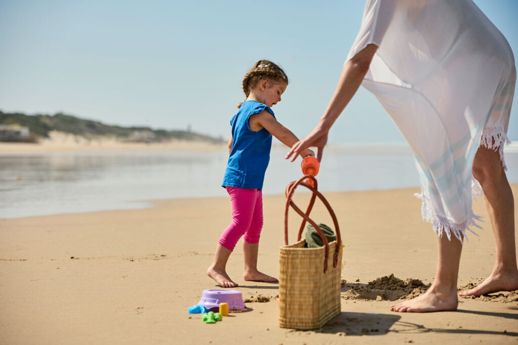 Kind und Mutter am Strand mit Tasche gepackt mit einer Packliste für den Sommerurlaub
