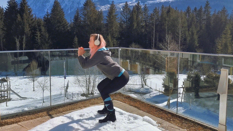 Frau macht Kniebeuge als Skigymnastik-Übung aus dem Stand