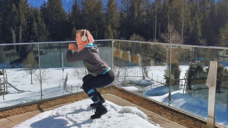 Frau macht Wadenheben in der Abfahrtshocke als Skigymnastik-Übung aus dem Stand